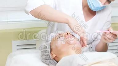 美容师将面霜涂在客户`脸颊上，做美容手术，清洁面部美容。